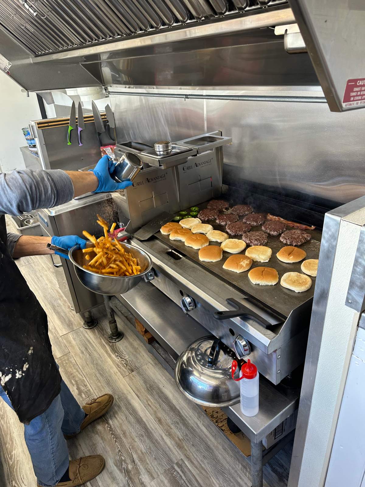 Cook tossing fresh fries while burgers sizzle on the griddle inside the truck