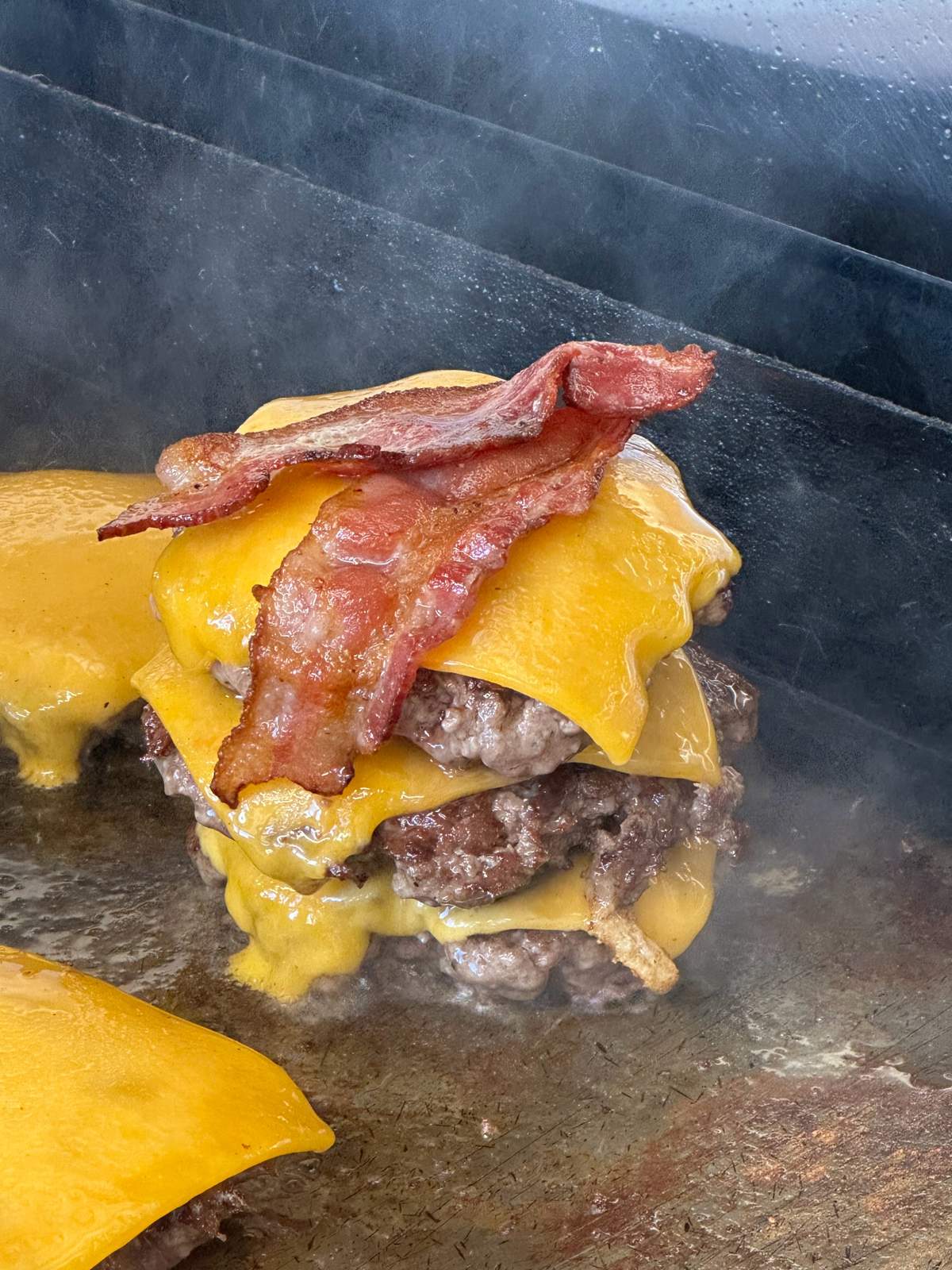Triple smash patties with melted cheese and bacon on the griddle